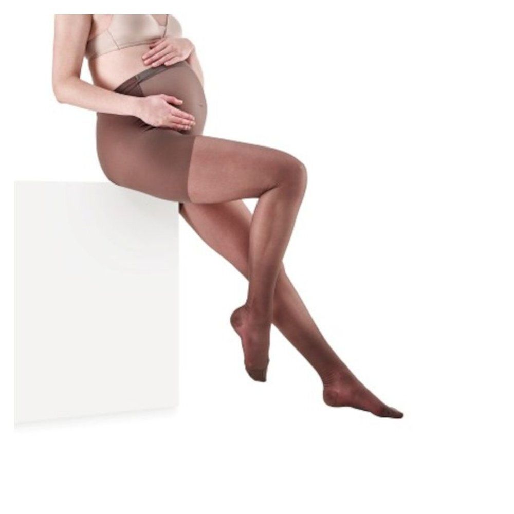 Collant de grossesse couleur chair. Vue d'une femme enceinte portant le collant. La femme est assise sur un cube blanc.