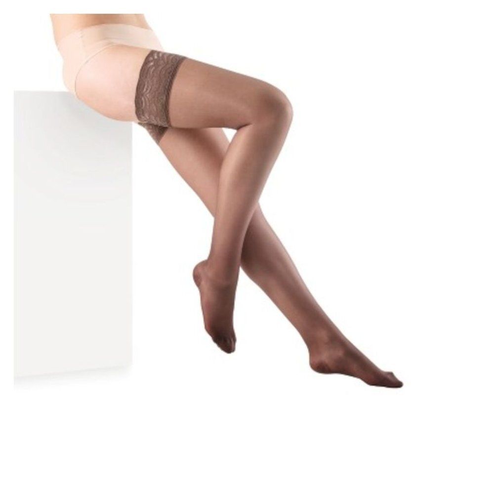 Bas sur fond blanc. Haut des cuisses avec dentelle. Couleur marron. Femme assise sur un bloc blanc.