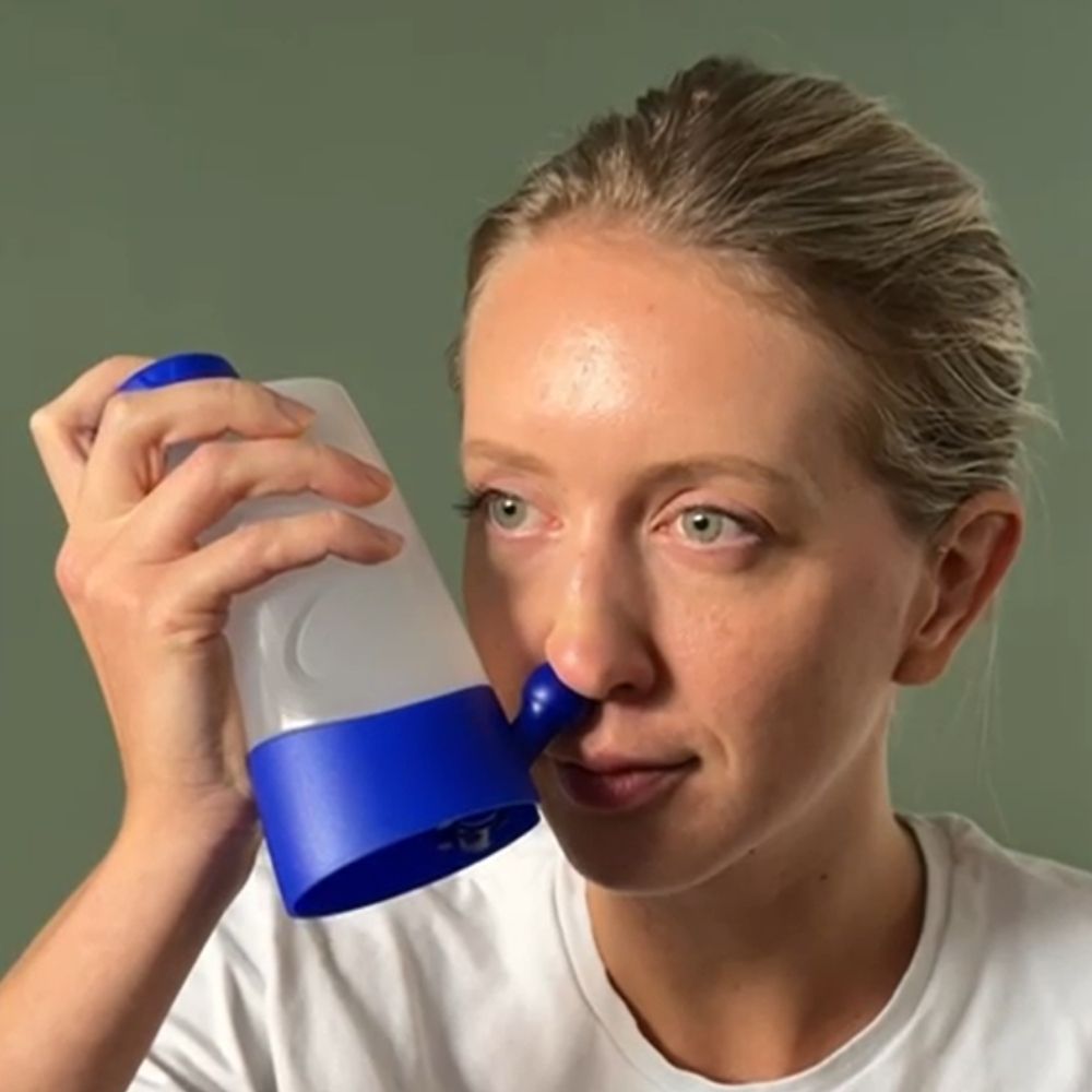 Gros plan d'une femme utilisant une douche nasale. Le produit a un couvercle et une base bleus.