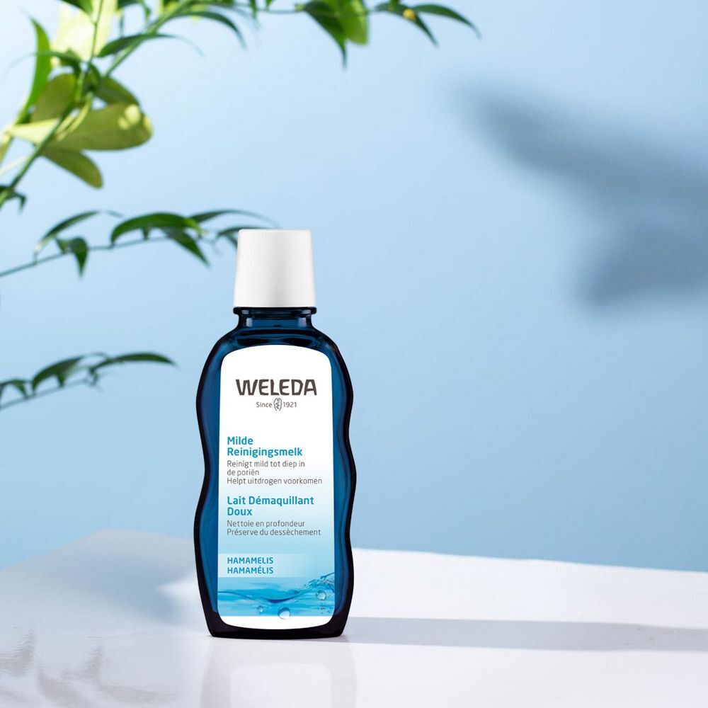 Bouteille bleue Weleda avec bouchon blanc. Informations sur le produit sur la bouteille. Fond avec eau et feuilles.