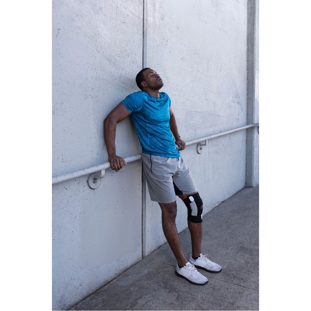 Genouillère. Noir et gris. Avec fermetures velcro. 3M™ Futuro™ Sport. Sur l'emballage, une personne porte la genouillère.