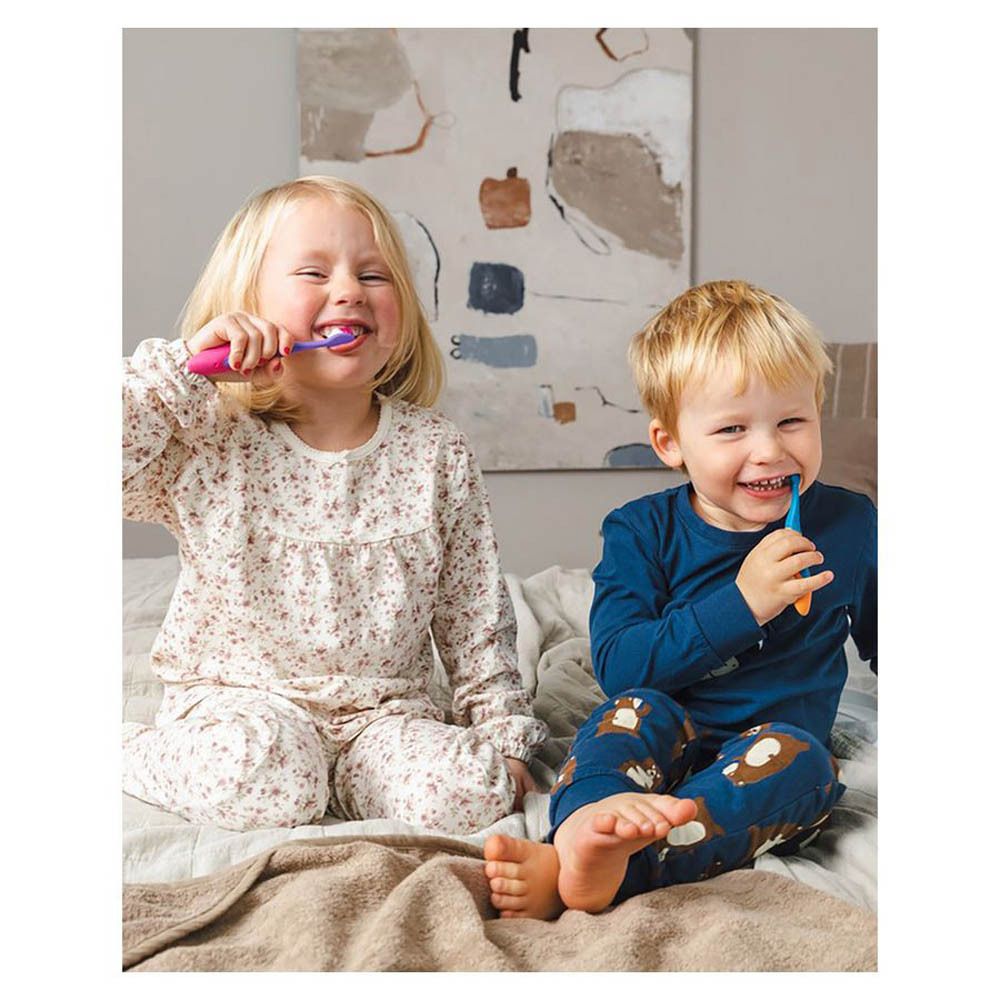 Deux enfants se brossent les dents avec des brosses à dents. Assis sur un lit.