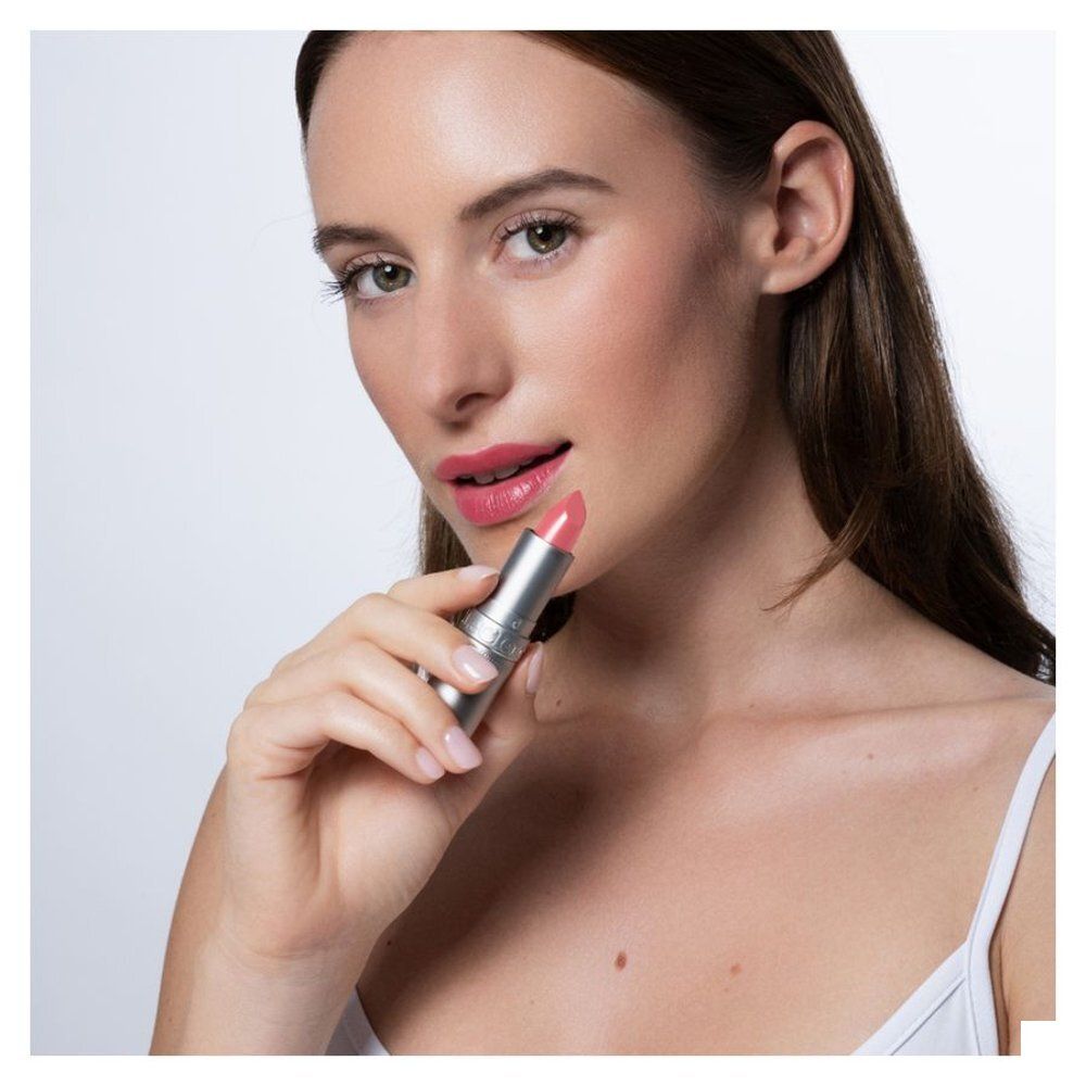 Femme tenant un rouge à lèvres transparent T. LeClerc. Elle porte du rouge à lèvres rose. Rouge à lèvres argenté.