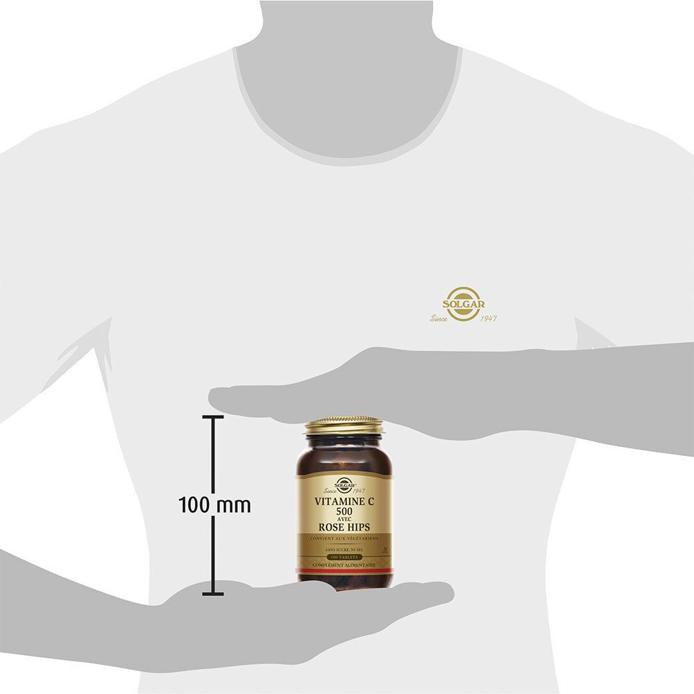 Personne tenant un flacon en verre brun. Le flacon mesure 100 mm de haut. Sur le flacon: Vitamine C 500 avec cynorrhodon.