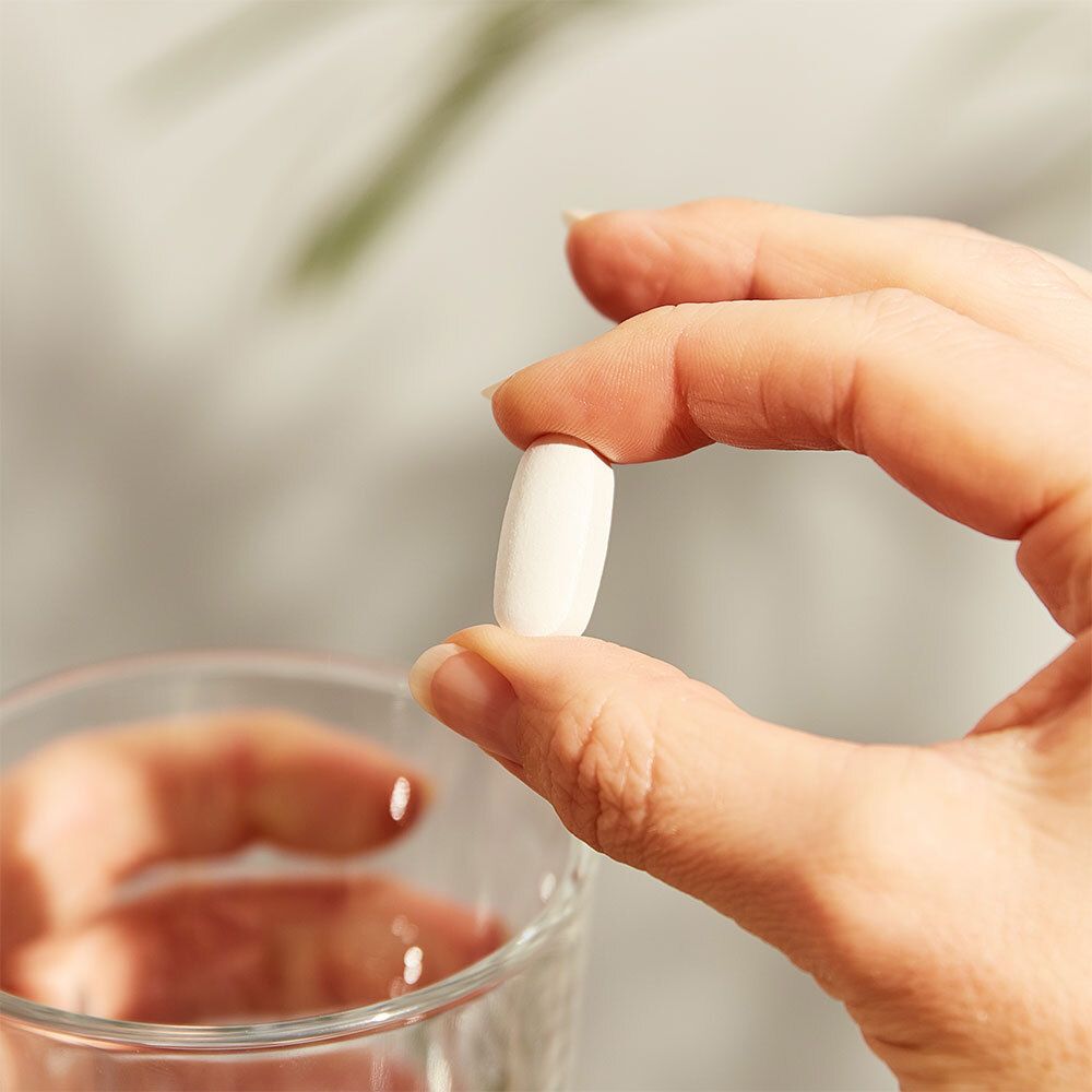 Main tenant un comprimé blanc ovale au-dessus d'un verre d'eau.