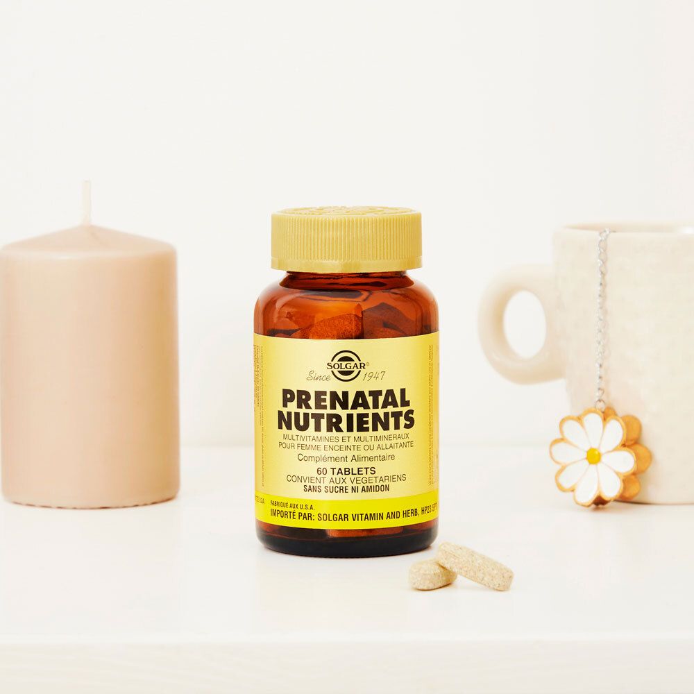 Flacon brun avec couvercle doré et deux comprimés. Inscription: Solgar Prenatal Nutrients. Sur table avec bougie et tasse.