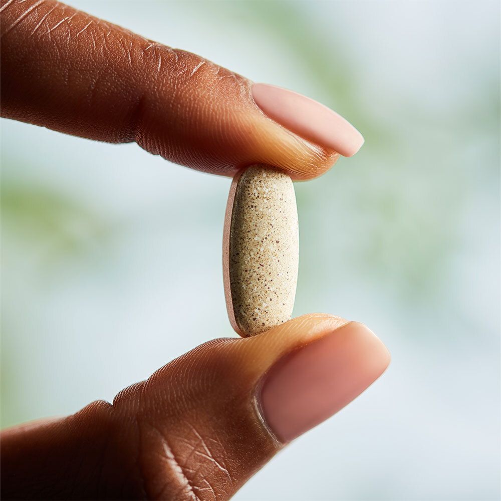 Un comprimé beige tenu entre deux doigts. Arrière-plan flou.