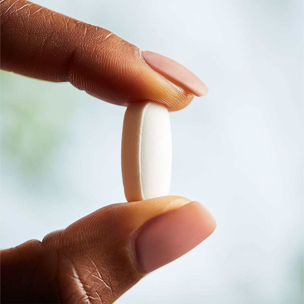 Main tenant un comprimé blanc ovale. Ongles roses. Vue rapprochée.