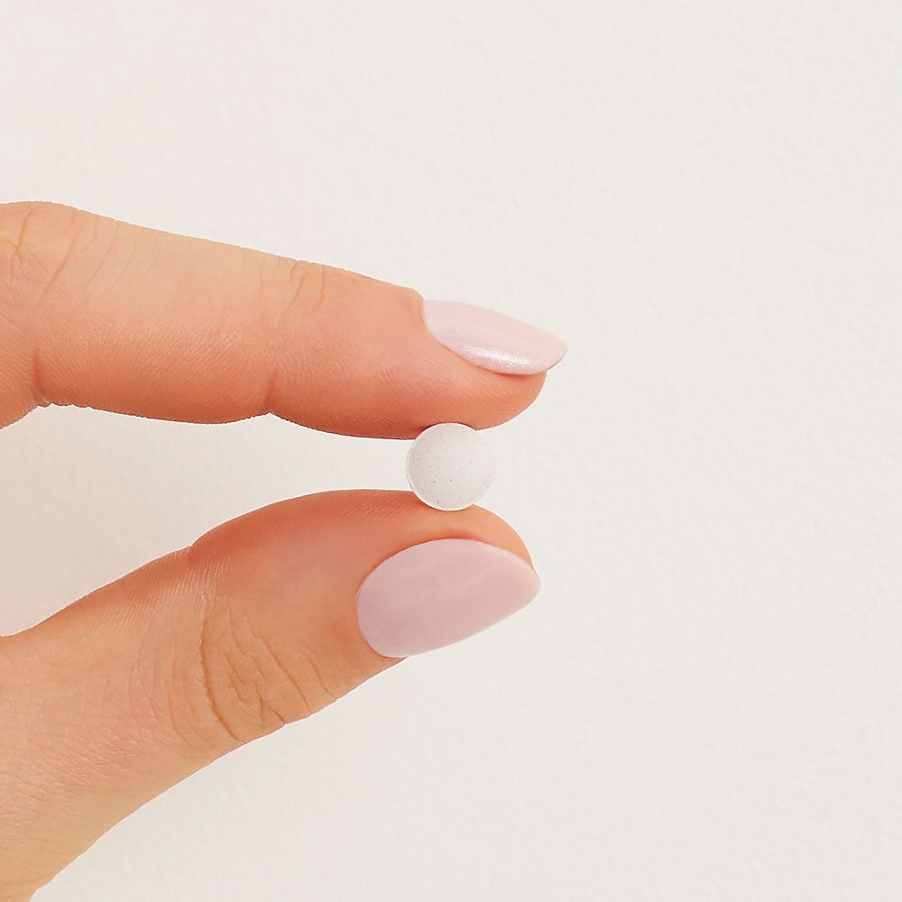 Un comprimé rond et blanc, tenu entre les doigts avec du vernis à ongles rose.