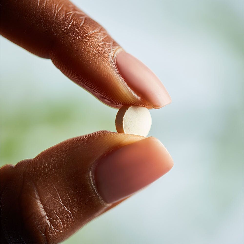 Main tenant un comprimé unique, rond et blanc entre les doigts.