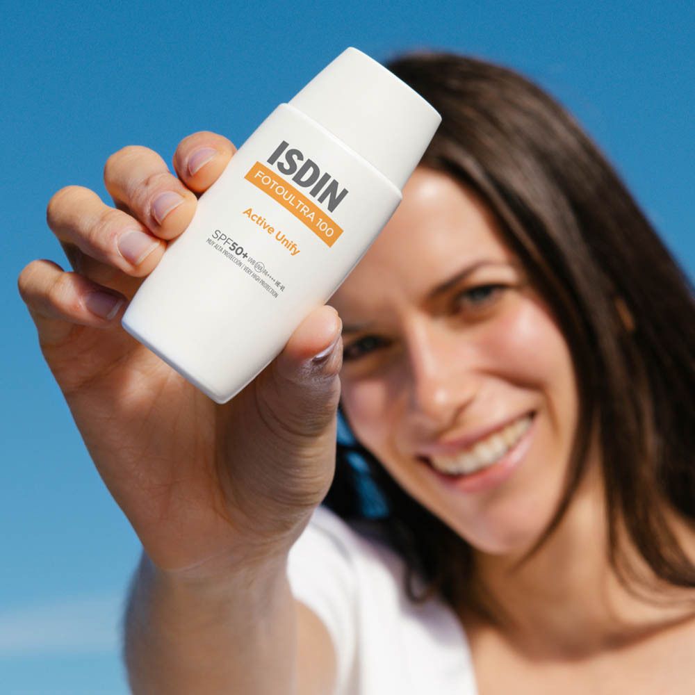 Femme tenant un flacon blanc. ISDIN FOTOULTRA 100 Active Unify SPF50+ est écrit dessus.