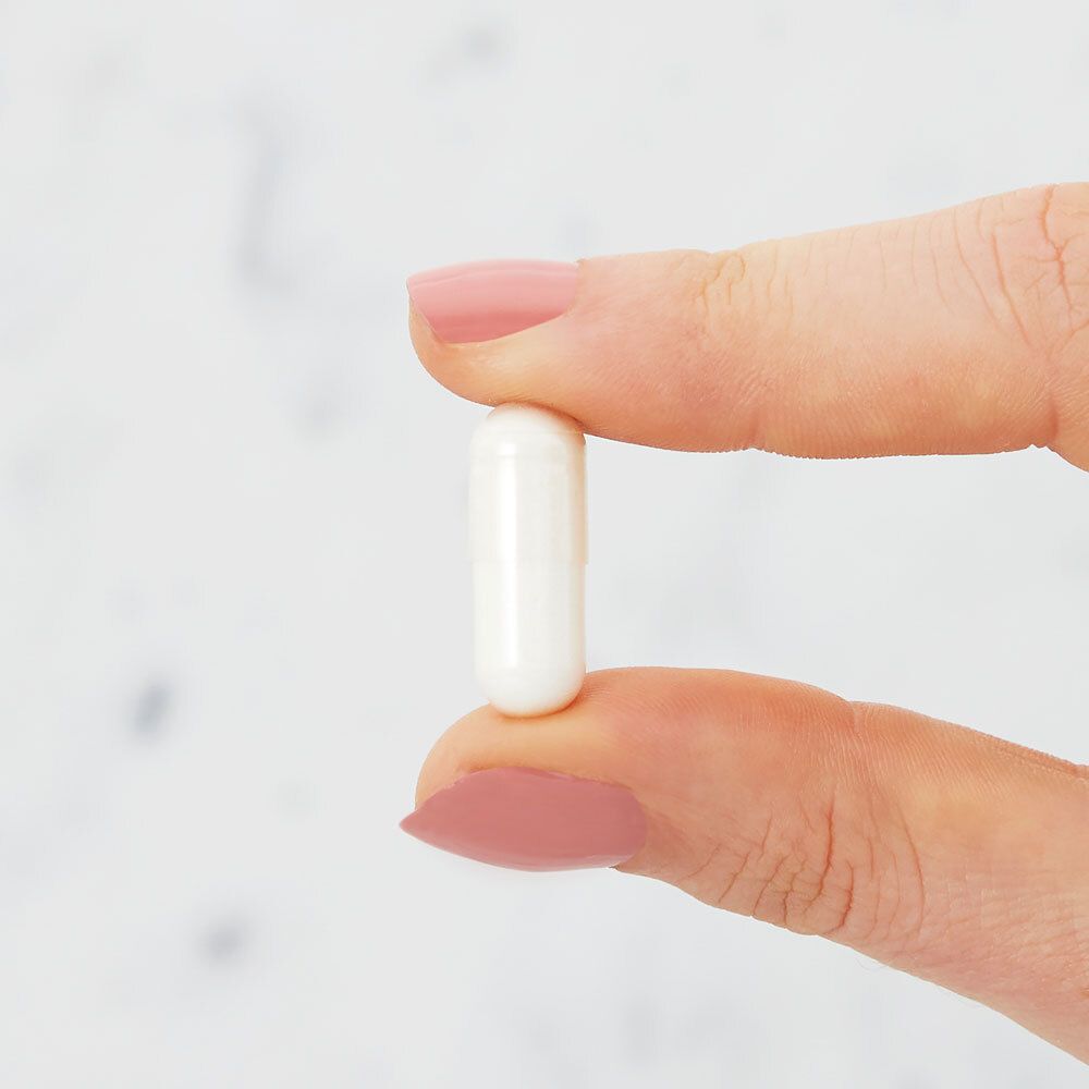 Une capsule blanche entre deux doigts. Fond flou.
