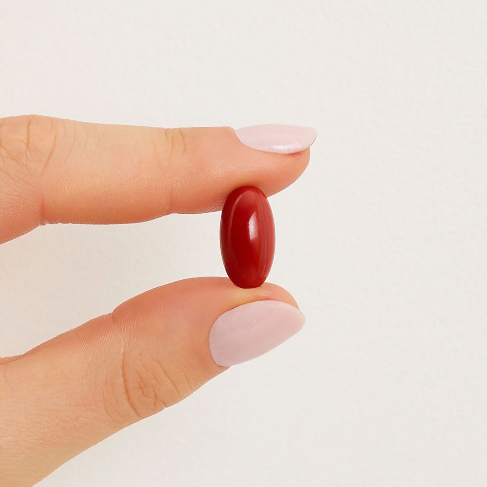 Une capsule rouge tenue entre deux doigts avec vernis à ongles rose.