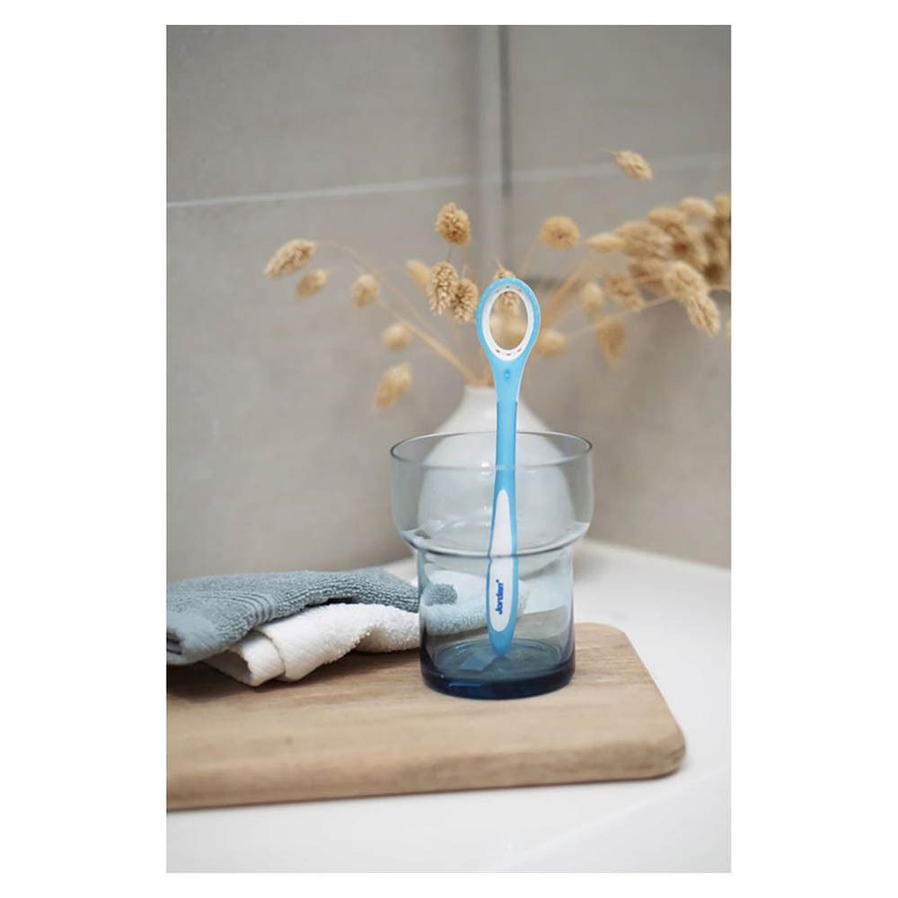 Nettoyeur de langue bleu dans un verre. Debout dans un verre d'eau. Sur une planche de bois. Dans la salle de bain.