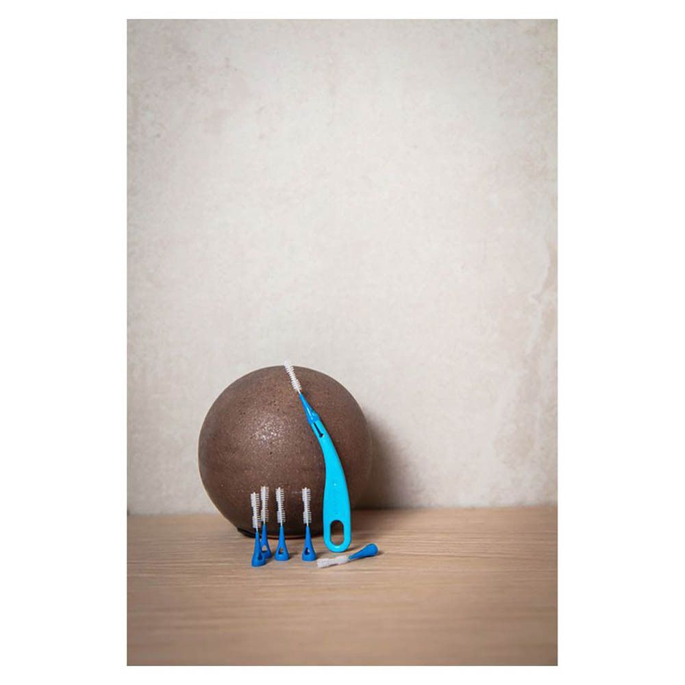 Brosse interdentaire Brush Between et recharges à côté d'un objet rond. Brosse individuelle et recharges.