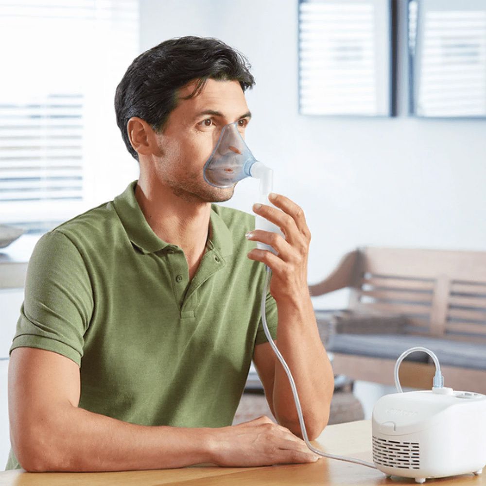 Homme portant un masque relié à un compresseur blanc. Il est assis à une table.