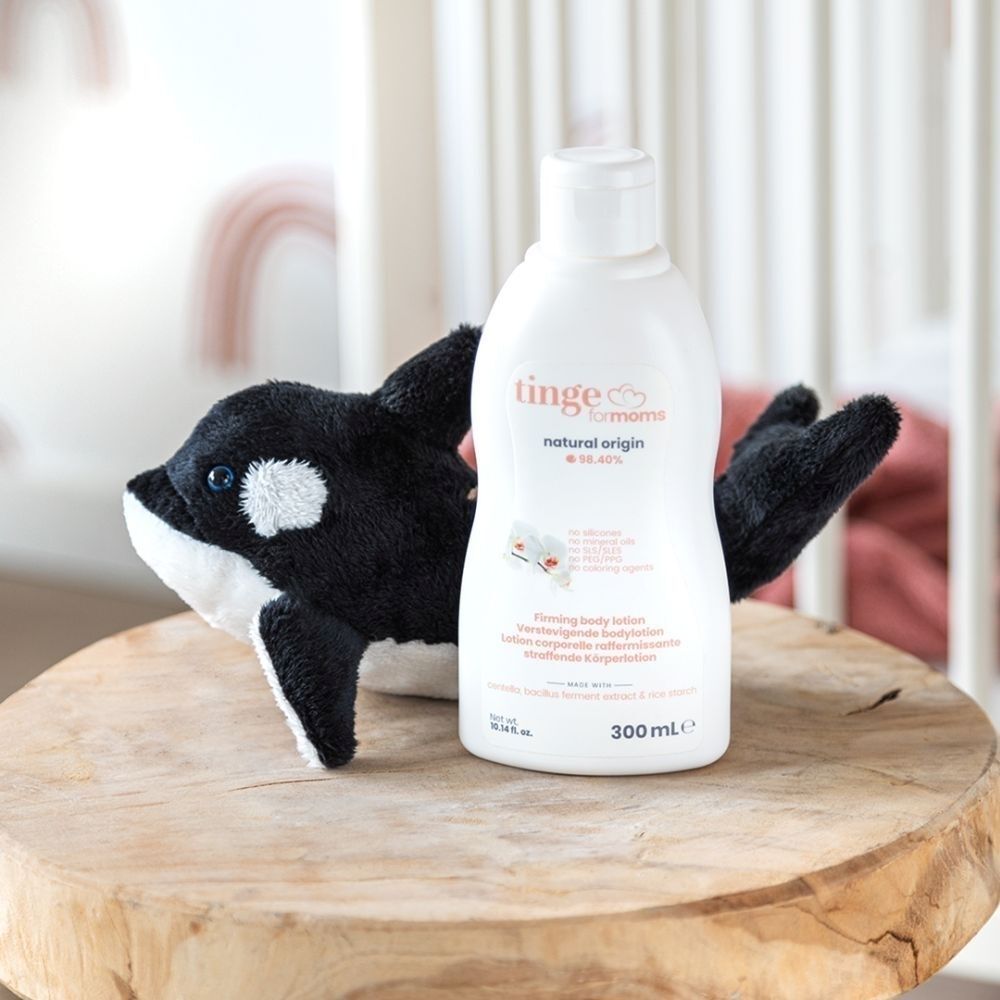 Bouteille de lotion pour le corps à côté d'une peluche orque sur une table en bois.