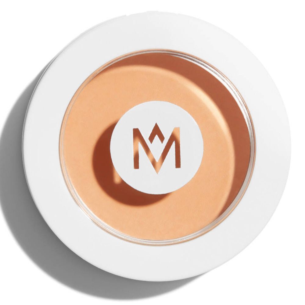 Boîtier rond blanc avec maquillage clair. Logo 'M' au centre. Couvercle avec fenêtre transparente.