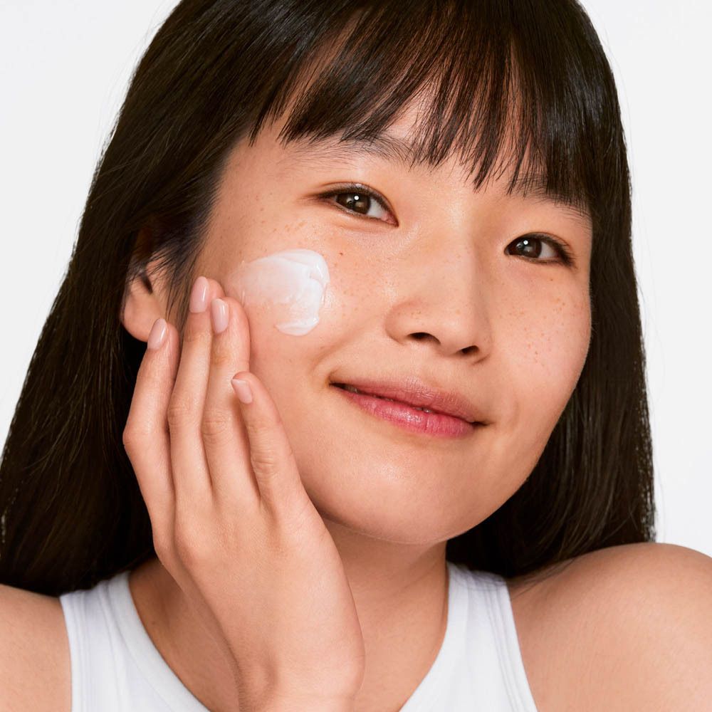 Une femme applique une crème blanche sur sa joue. La crème est clairement visible sur l'image.