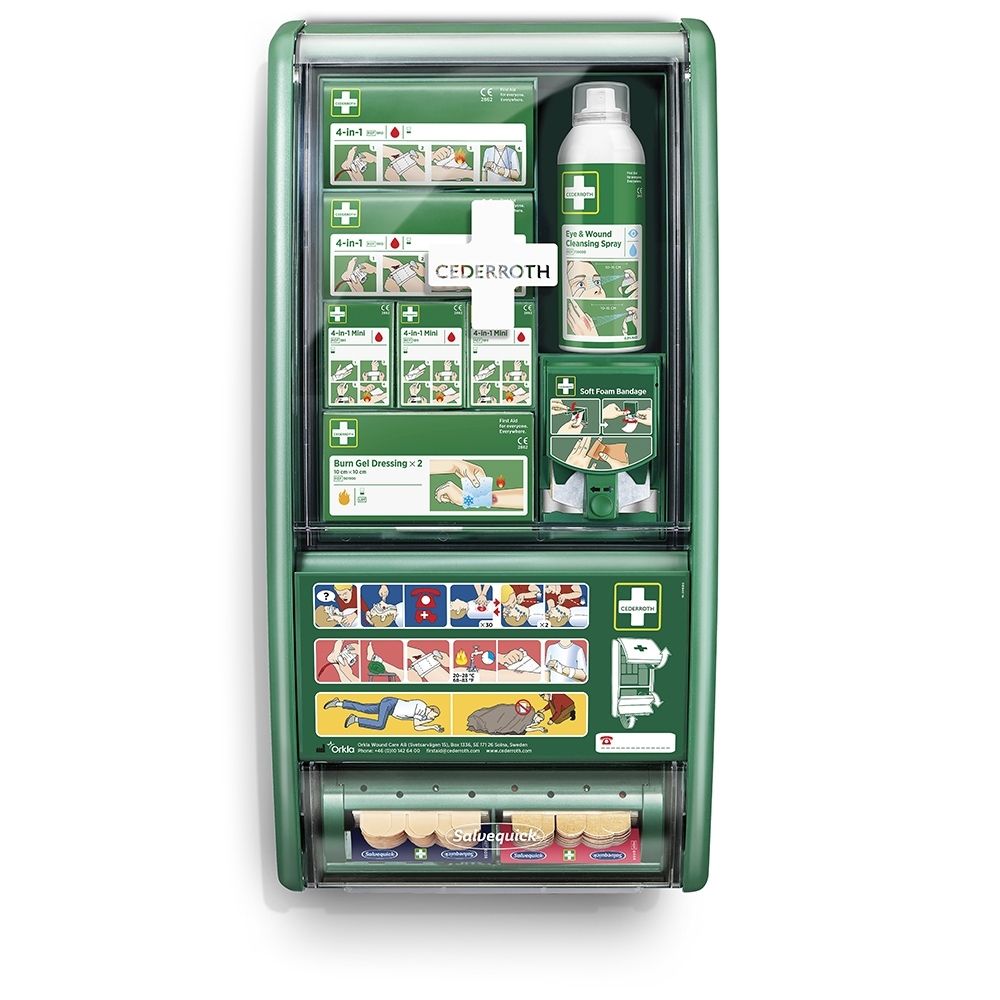 Station de premiers secours verte avec couvercle transparent, remplie de matériel de premiers secours et d'instructions.