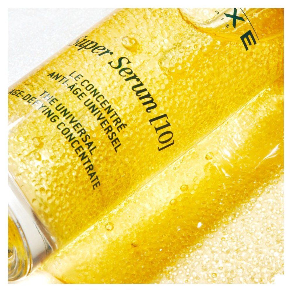 Gros plan du sérum concentré Nuxe Super Serum jaune avec des billes et des bulles.