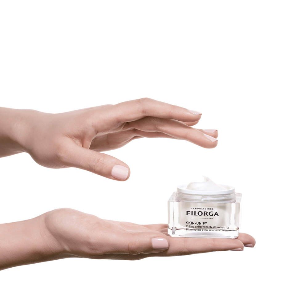 Mains tenant un pot de crème. Marque FILORGA. Nom du produit SKIN-UNIFY.