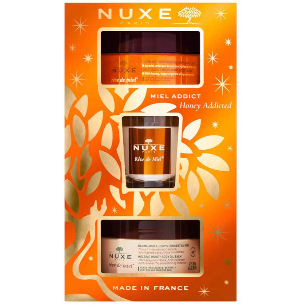 Coffret cadeau orange avec trois produits Nuxe. Contient des pots et un verre avec l'inscription Nuxe.  'Miel Addict' est visible.