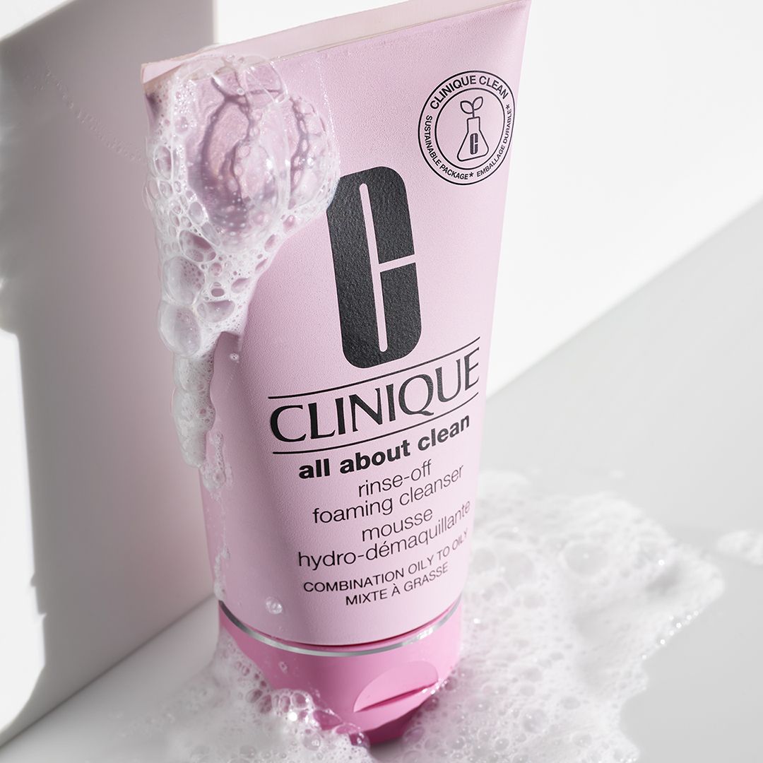 Tube rose CLINIQUE nettoyant moussant. Mousse autour du tube. Texte : all about clean rinse-off foaming cleanser.