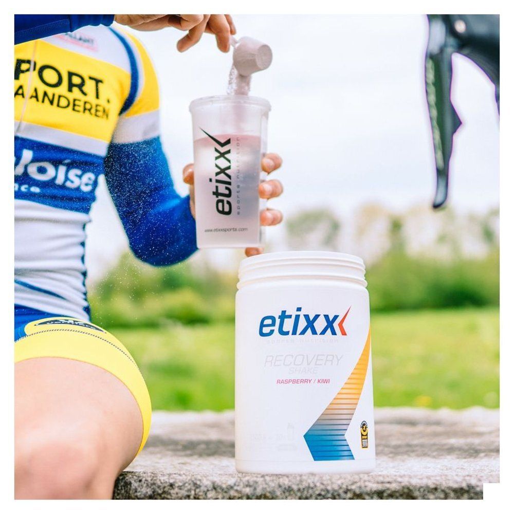 Personne tenant un shaker et un pot etixx Recovery Shake framboise/kiwi. Logo visible.