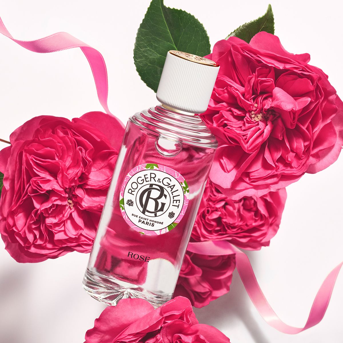 Flacon en verre avec bouchon blanc, entouré de roses. Texte: ROGER & GALLET, ROSE. Produit en détail.
