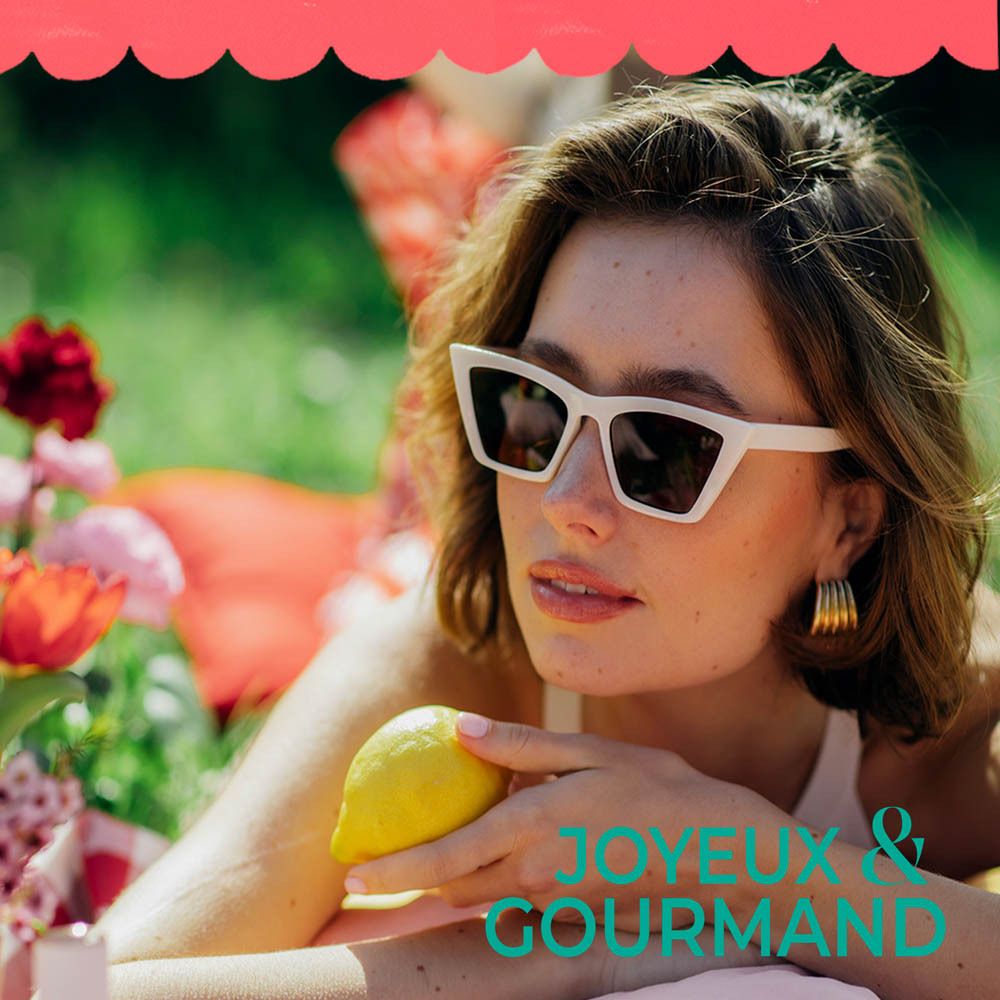 Femme avec des lunettes de soleil tenant un citron. Texte: JOYEUX & GOURMAND.
