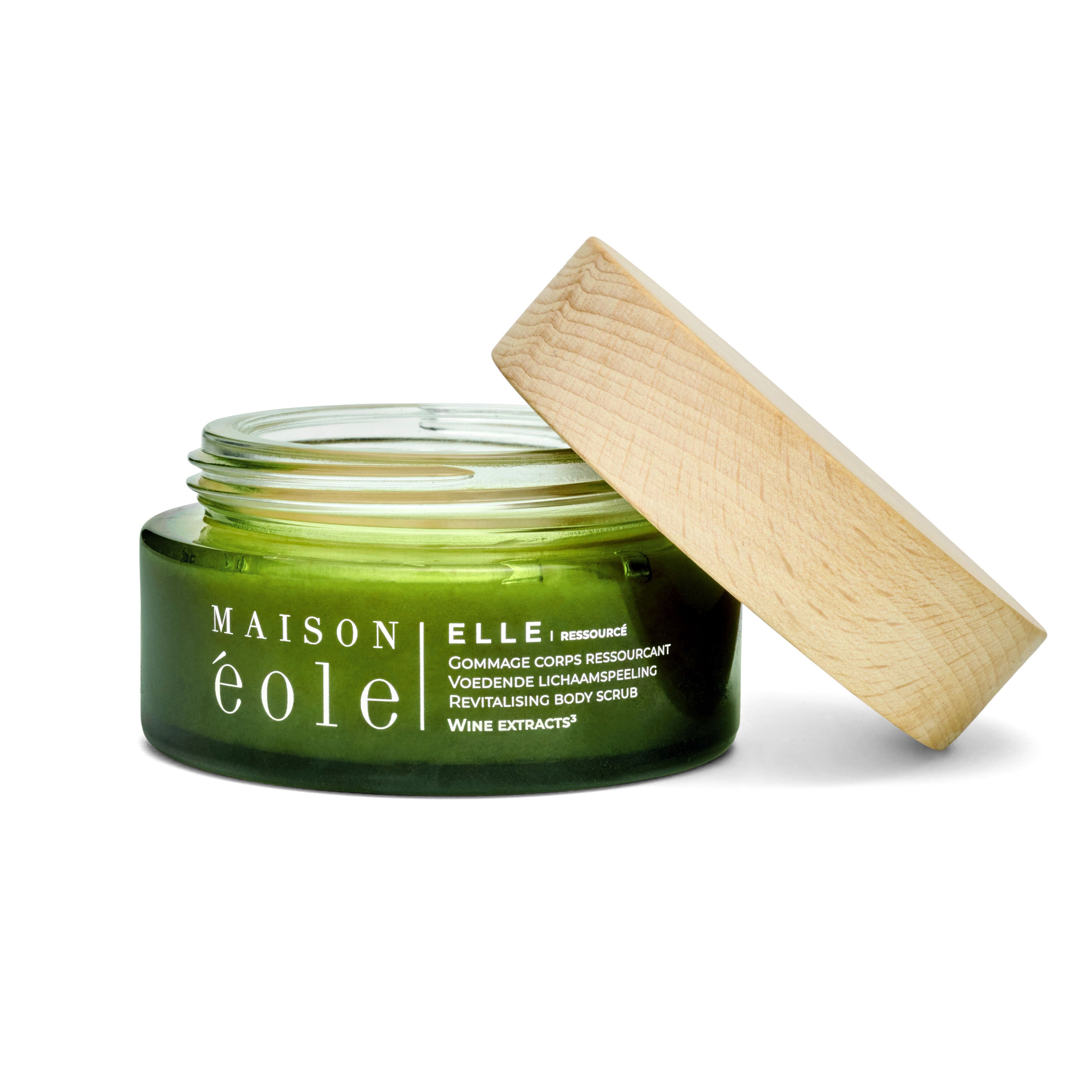 Pot en verre vert avec couvercle en bois, couvercle ouvert. Inscription: Maison Éole, Gommage Corps Ressourçant, Revitalising Body Scrub.