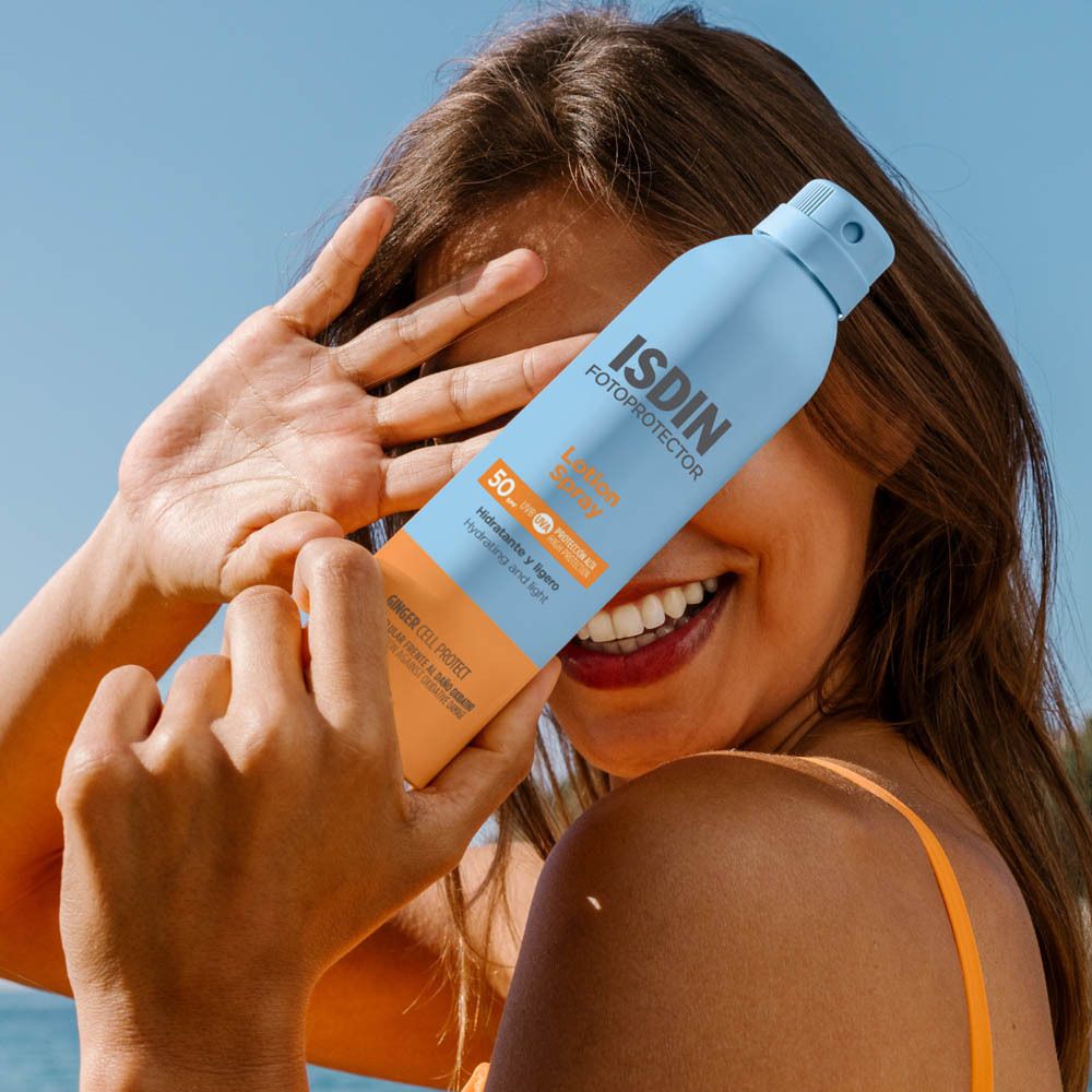 Femme tenant ISDIN Fotoprotector Lotion Spray SPF 50. Flacon bleu-orange. Sourit.
