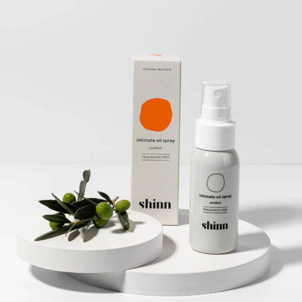 Produit, emballage, branche d'olivier. Texte : Intimate oil spray, sans parfum. Cercle orange.