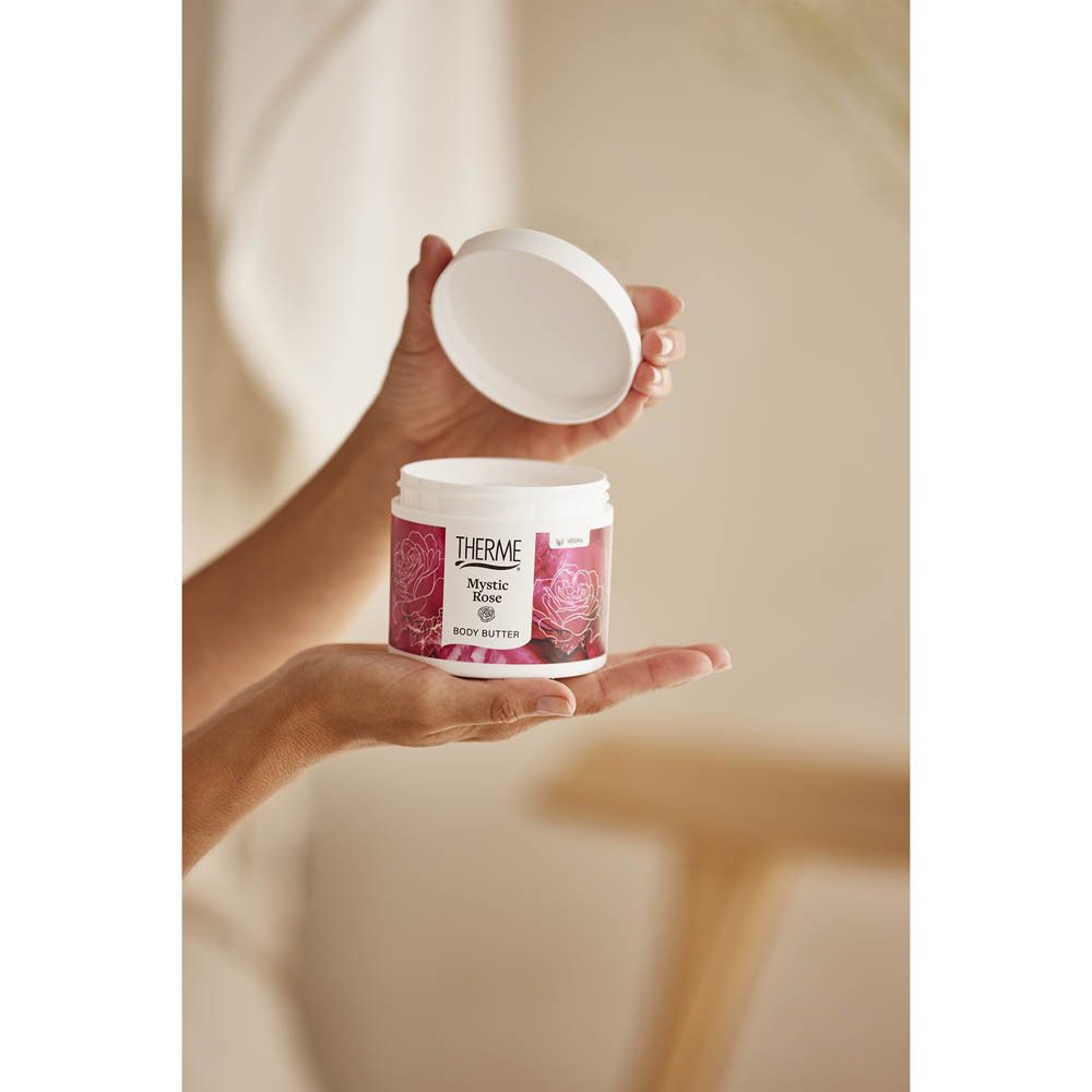 Personne tenant un pot blanc avec bande rouge. Inscription THERME, Mystic Rose, Body Butter. Couvercle ouvert.