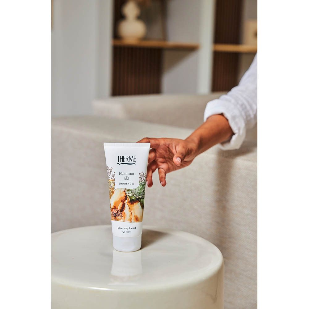 Main tenant un tube blanc THERME Hammam Shower Gel. Le produit est pressé dans la paume.