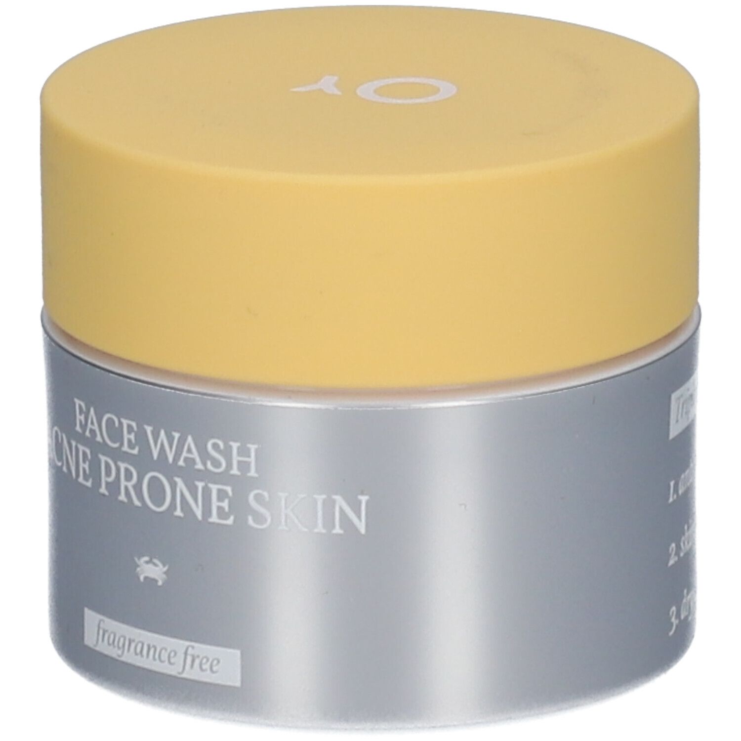 Pot de crème avec couvercle jaune et contenant argenté. Inscription 'FACE WASH ACNE PRONE SKIN' et logo OY.