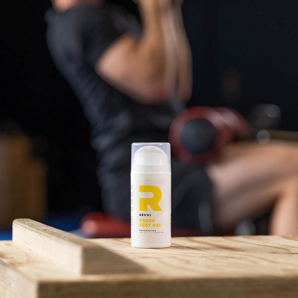 Petit flacon RÉVVI FRESH FEET GEL. "R" jaune et pompe jaune. En arrière-plan, une personne s'entraînant.