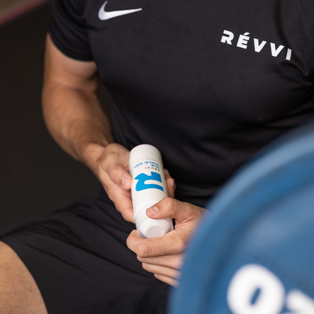 Personne tenant un flacon blanc avec logo "R" bleu et texte: RÉVVI ICE COLD GEL. T-shirt noir.
