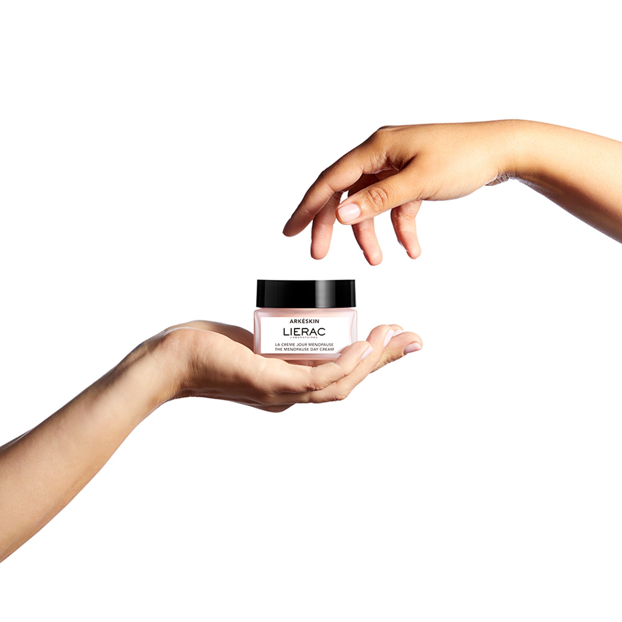 Mains tenant un pot de crème. Étiquette : Arkéskin, LIERAC, La Crème Jour Ménopause, The Menopause Day Cream.