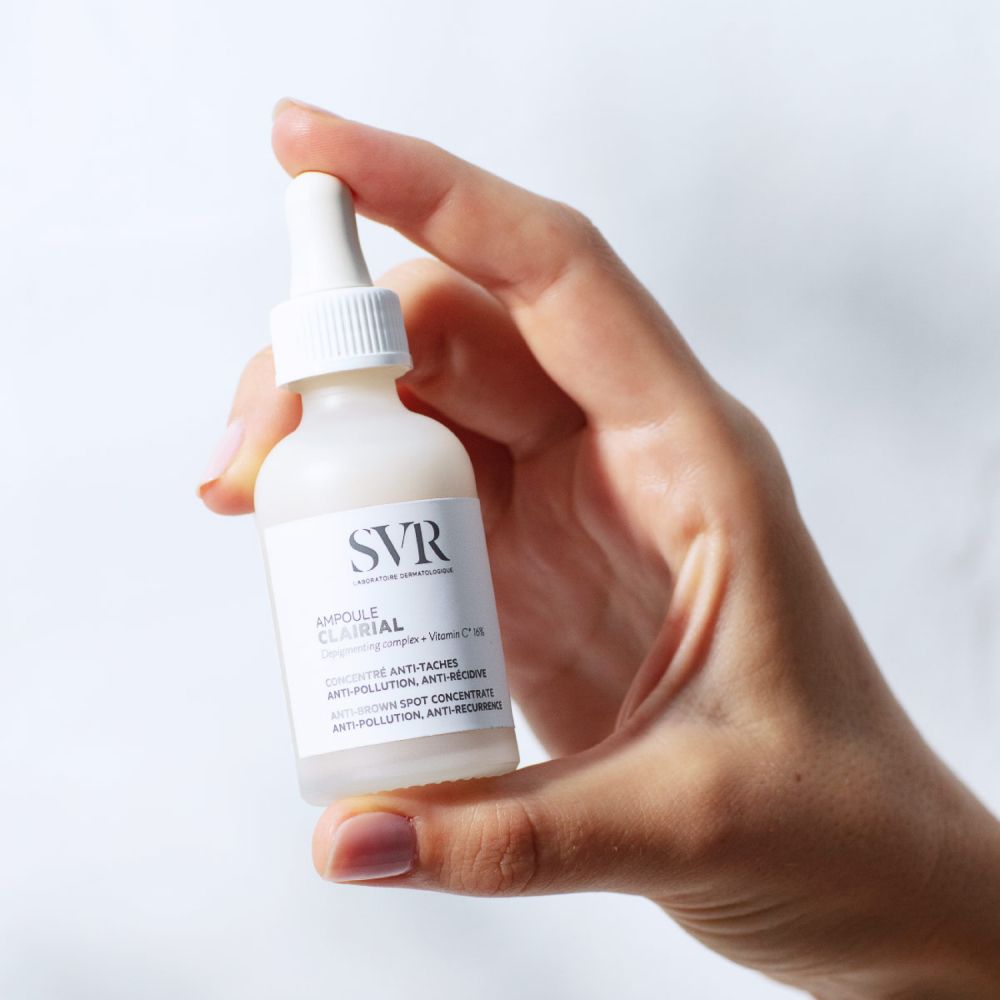 Main tenant un flacon avec pipette. Inscription: SVR, Ampoule Clairial, Anti-Taches, Anti-Récidive.