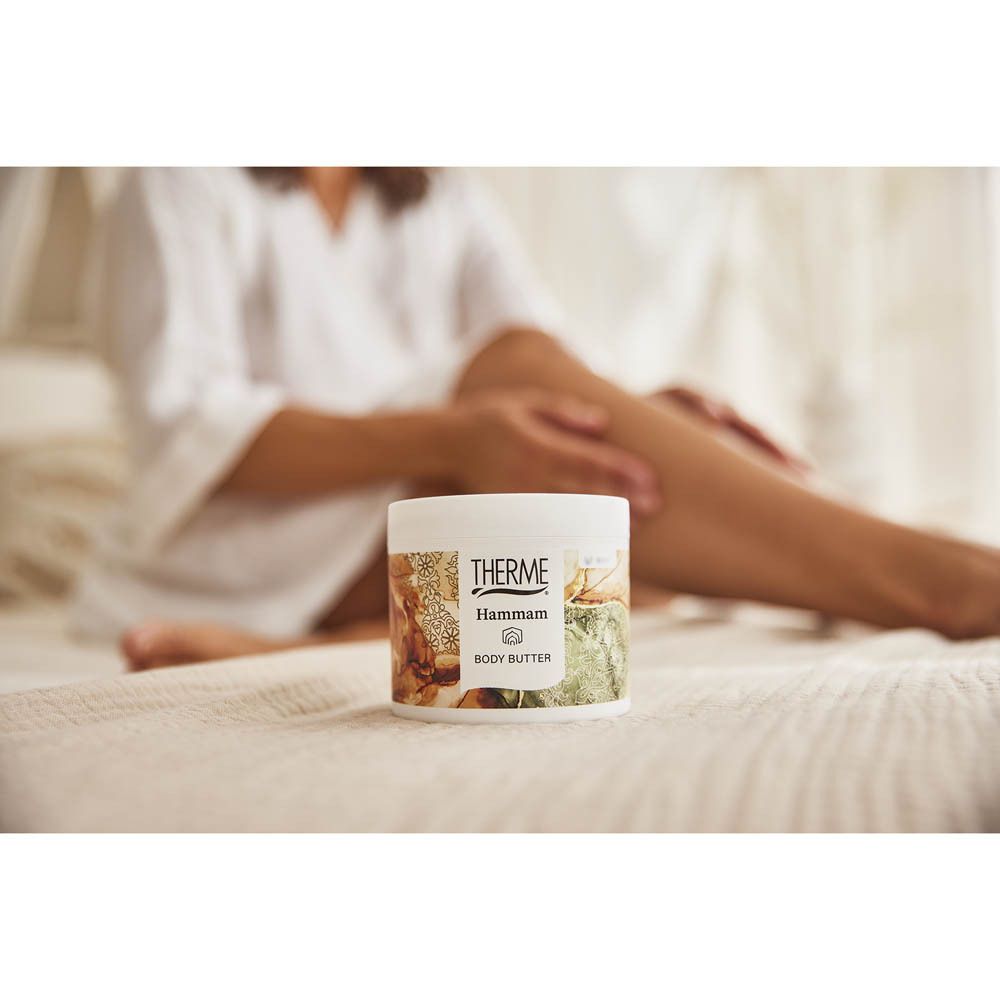 Personne assise sur un lit. THERME Hammam BODY BUTTER sur le lit.