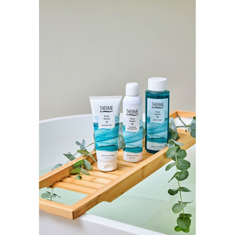 Plusieurs produits THERME Finn Sauna, dont du gel douche, sur un plateau de baignoire en bois.