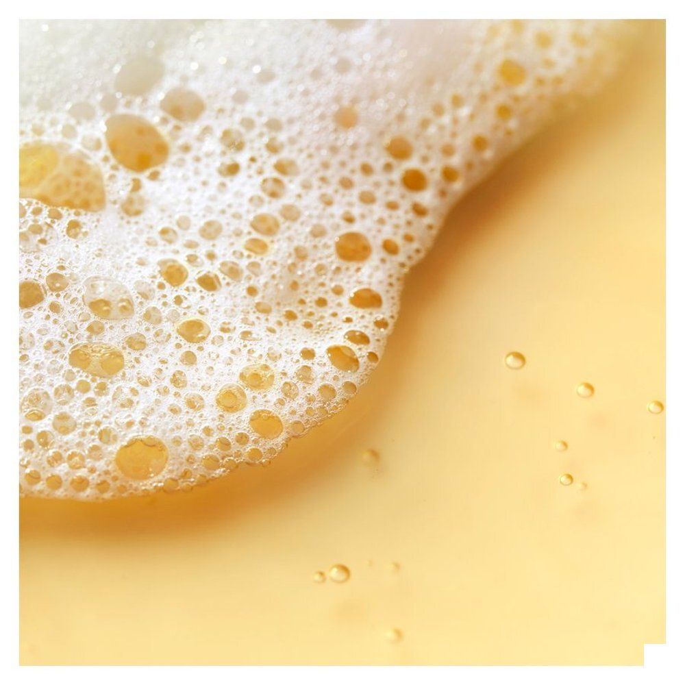 Gros plan de mousse et de liquide jaune, Shampooing Après-Soleil Nuxe.