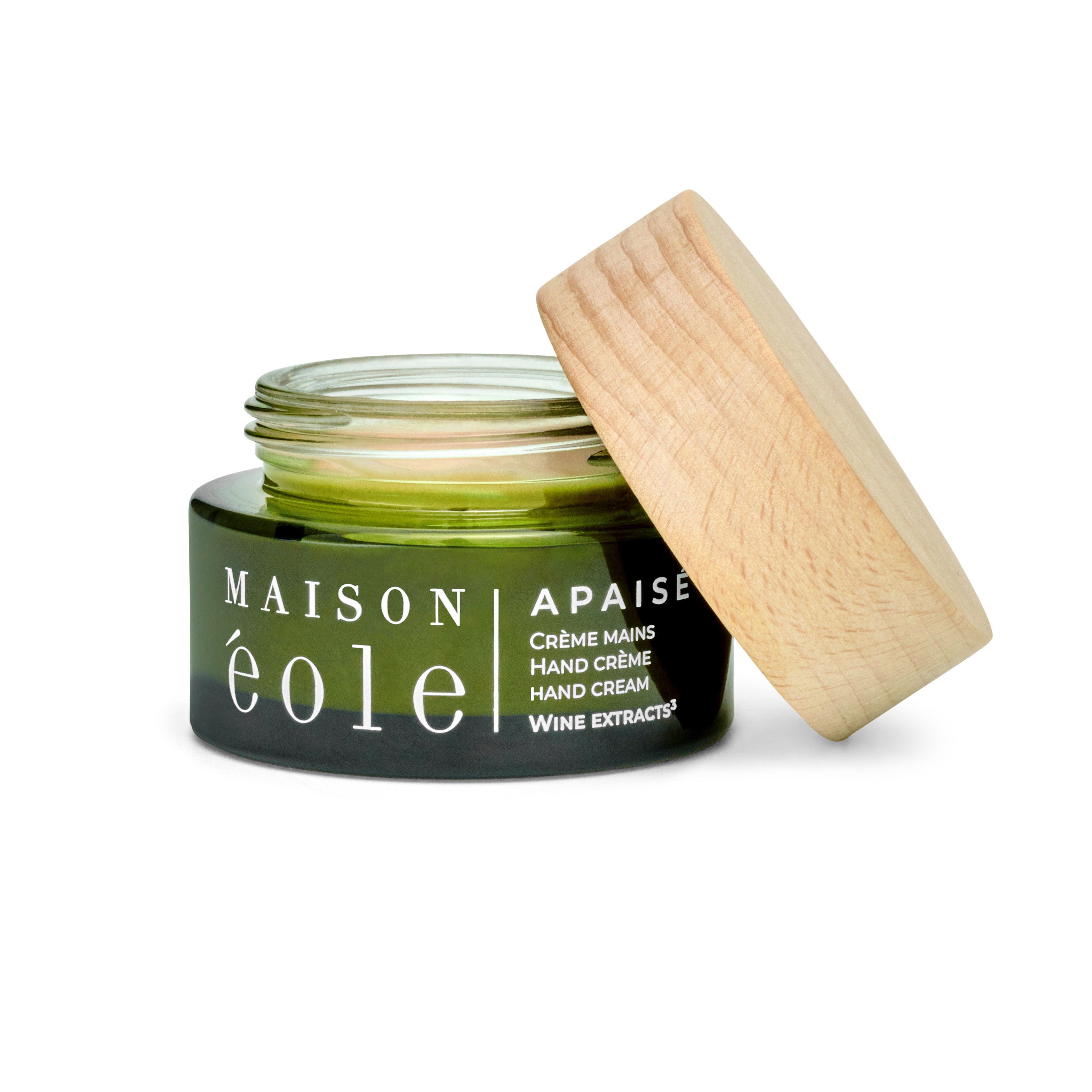 Pot de crème en verre vert avec couvercle en bois. Couvercle à côté. Inscription : Maison Éole, Apaisé, Crème Mains, Hand Crème, Hand Cream, Wine Extracts.
