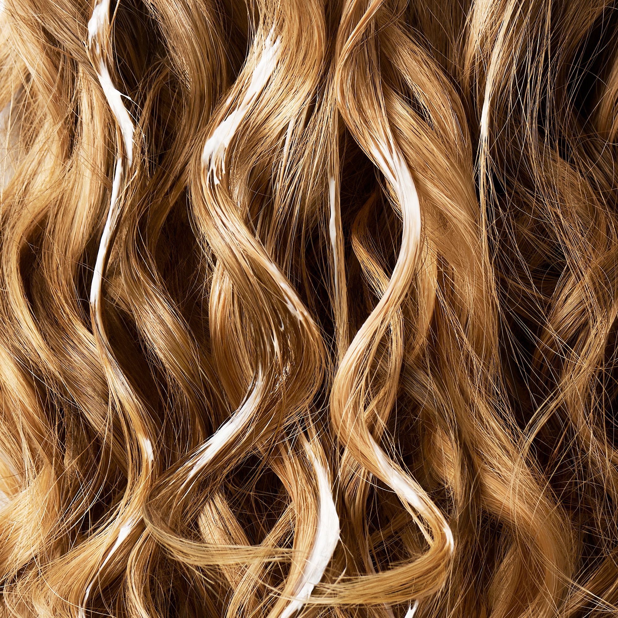 Mèches de cheveux avec substance blanche. Cheveux bouclés, châtain clair. La substance semble appliquée.