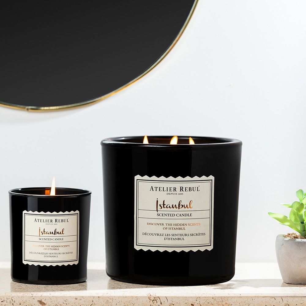 Deux bougies noires. Étiquette avec texte: Atelier Rebul Istanbul Scented Candle. Une brûle.