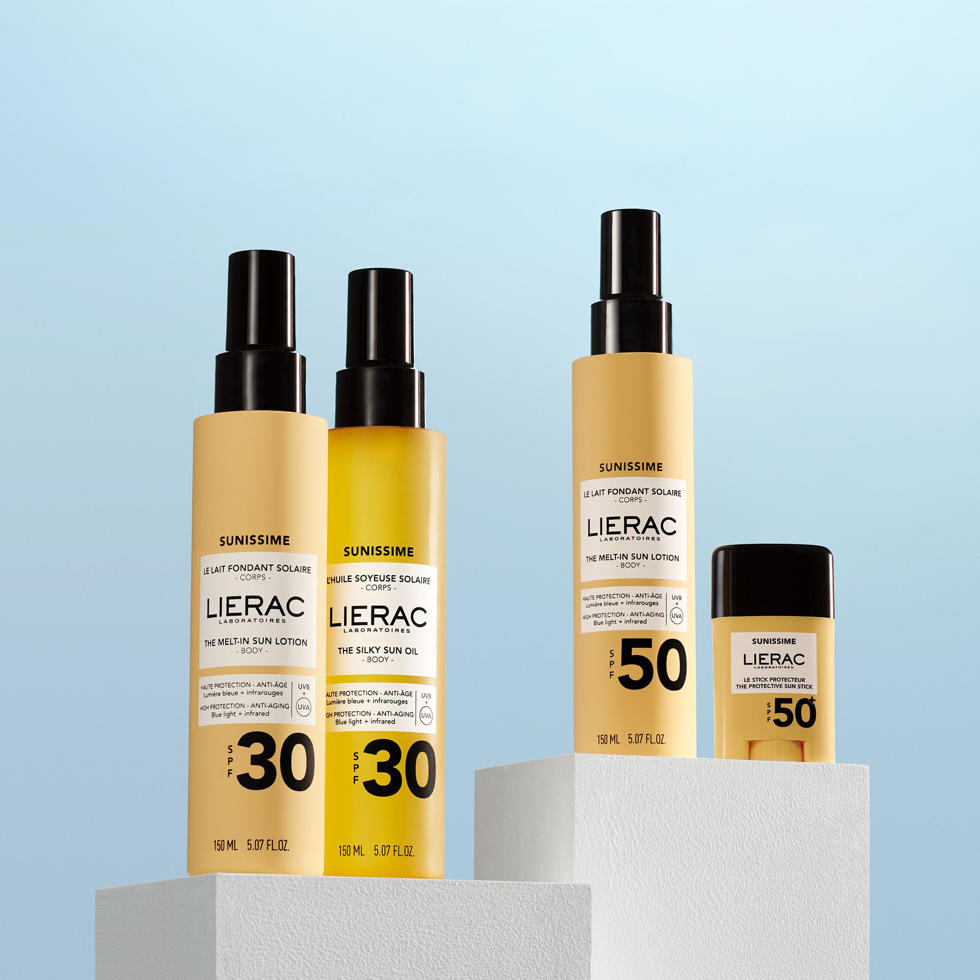 Plusieurs produits LIERAC SUNISSIME. Lotion solaire SPF50, huile SPF30, stick SPF50. Sur blocs blancs.