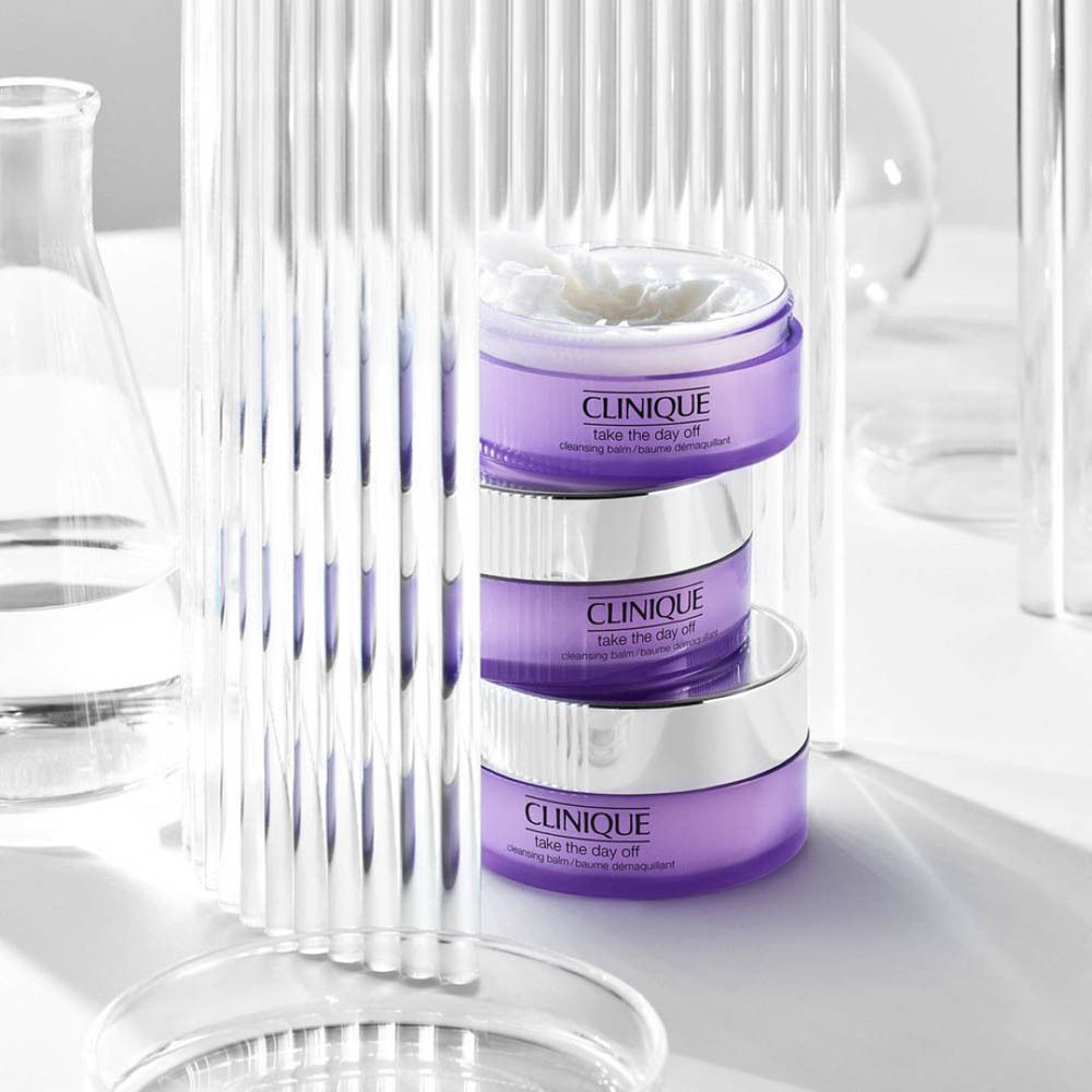 Trois pots CLINIQUE Take the Day Off, empilés. Verrerie et matériel de laboratoire en arrière-plan.