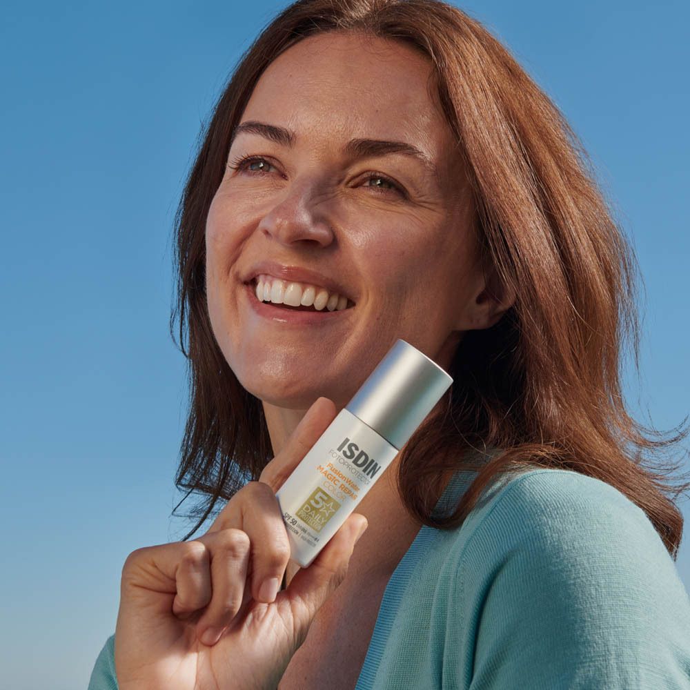 Femme tenant un flacon. Inscription: ISDIN Fotoprotector Fusion Water Magic Repair Color SPF50.